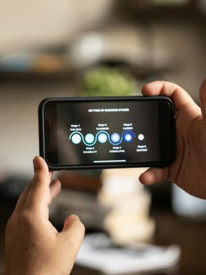 Hands holding a smartphone displaying business stages in a cozy indoor setting.